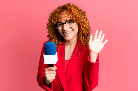 Photo for Red hair pretty woman smiling happily, waving hand, welcoming and greeting you. journalist and presenter concept - Royalty Free Image