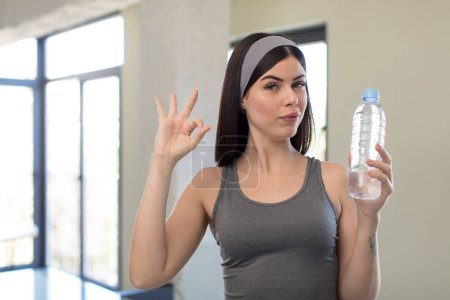 Téléchargez les photos : Jolie jeune femme se sentant heureuse, montrant l'approbation avec le geste correct. concept de bouteille d'eau - en image libre de droit