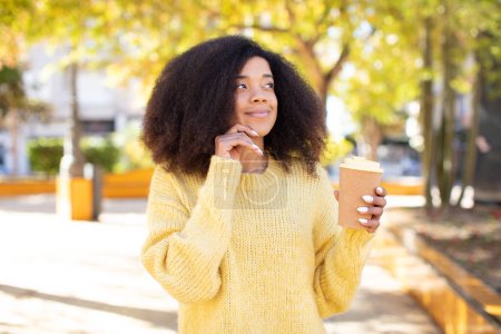 Foto de Bonita mujer negra afro sonriendo con una expresión feliz y segura con la mano en la barbilla. quitar el concepto de café - Imagen libre de derechos