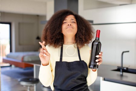 Photo for Pretty afro black woman crossing fingers and hoping for good luck. wine bottle concept - Royalty Free Image