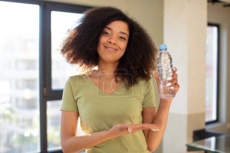 Photo for Pretty afro black woman smiling cheerfully, feeling happy and showing a concept. water bottle concept - Royalty Free Image