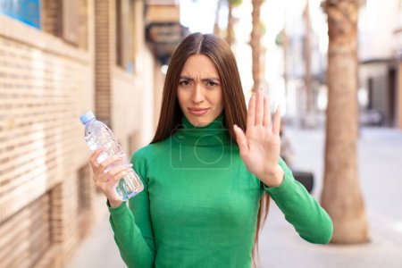 Photo for Looking serious showing open palm making stop gesture. water bottle concept - Royalty Free Image