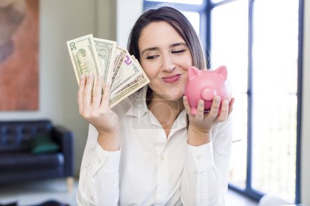 Foto de Young adult pretty woman with a piggy bank. money and savings concept - Imagen libre de derechos