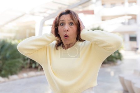 Photo for Middle age woman looking excited and surprised, open-mouthed with both hands on head, feeling like a lucky winner - Royalty Free Image