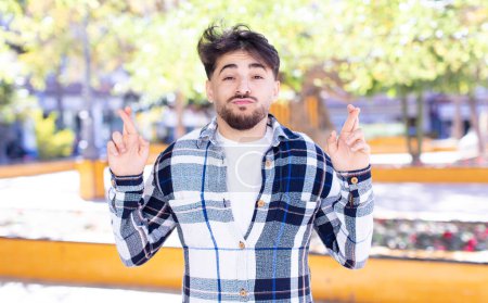 Téléchargez les photos : Jeune homme beau croisant les doigts anxieusement et espérant bonne chance avec un regard inquiet - en image libre de droit
