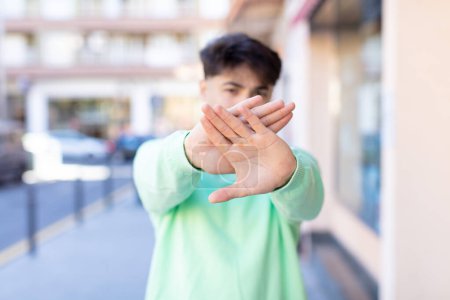 Photo for Young handsome man covering face with hand and putting other hand up front to stop camera, refusing photos or pictures - Royalty Free Image
