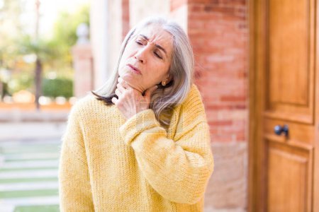 Téléchargez les photos : Senior retraité jolie femme aux cheveux blancs se sentant malade avec un mal de gorge et des symptômes de grippe, toux avec la bouche couverte - en image libre de droit