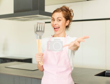Foto de Joven bonita mujer sonriendo felizmente y ofreciendo o mostrando un concepto. concepto de chef casero - Imagen libre de derechos
