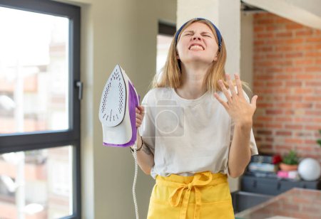 Photo for Young pretty woman screaming with hands up in the air.  iron and clothes concepts - Royalty Free Image