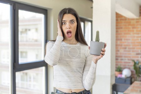 Photo for Pretty young model feeling extremely shocked and surprised. decorative cactus concept - Royalty Free Image