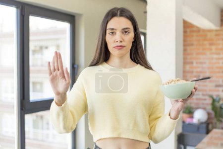 Foto de Modelo bastante joven mirando serio mostrando palmera abierta haciendo gesto de parada. concepto de plato de desayuno - Imagen libre de derechos