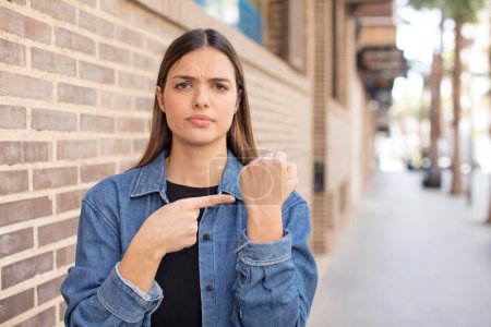Photo for Young pretty woman looking impatient and angry, pointing at watch, asking for punctuality, wants to be on time - Royalty Free Image