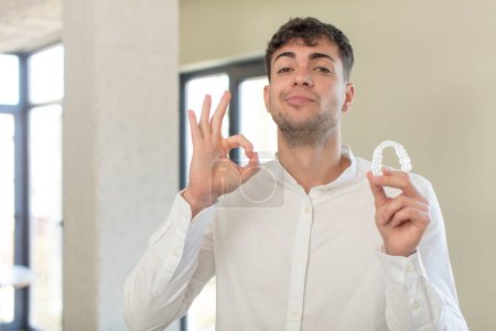 Photo for Young handsome man feeling happy, showing approval with okay gesture. dental retainer concept - Royalty Free Image