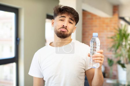 Foto de Joven hombre guapo sintiéndose triste y llorón con una mirada infeliz y llorando. concepto de botella de agua - Imagen libre de derechos