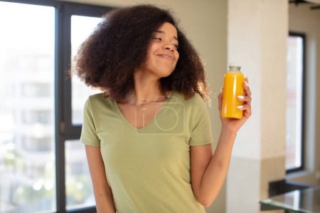 Foto de Bonita mujer negra afro sonriendo y mirando con una expresión de confianza feliz. concepto de zumo de naranja - Imagen libre de derechos