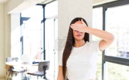 Photo for Young adult pretty woman covering eyes with one hand feeling scared or anxious, wondering or blindly waiting for a surprise - Royalty Free Image