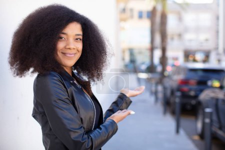 Téléchargez les photos : Afro-américaine jolie femme se sentant heureuse et joyeuse, souriante et accueillante, vous invitant à entrer avec un geste amical - en image libre de droit