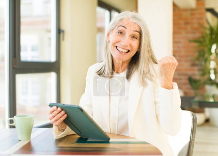Téléchargez les photos : Senior jolie femme se sentant choqué, rire et célébrer le succès avec un écran tactile - en image libre de droit