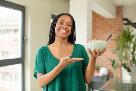 Téléchargez les photos : Noir afro femme souriant joyeusement, se sentant heureux et montrant un concept. concept bol petit déjeuner - en image libre de droit