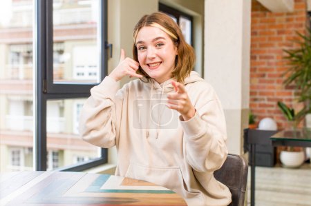 Foto de Pretty caucasian woman smiling cheerfully and pointing to camera while making a call you later gesture, talking on phone. home interior concept - Imagen libre de derechos