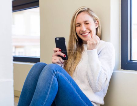 Foto de Young adult pretty blonde woman using her smartphone at home - Imagen libre de derechos