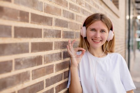 Foto de Joven bonita mujer sintiéndose feliz, mostrando aprobación con buen gesto. auriculares y concepto de música - Imagen libre de derechos