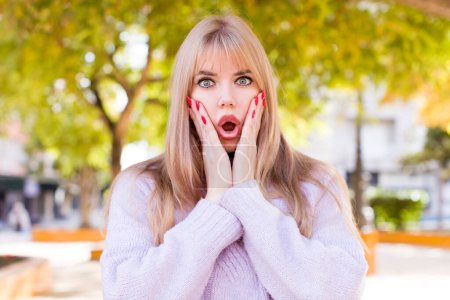 Photo for Young pretty woman feeling shocked and scared, looking terrified with open mouth and hands on cheeks - Royalty Free Image