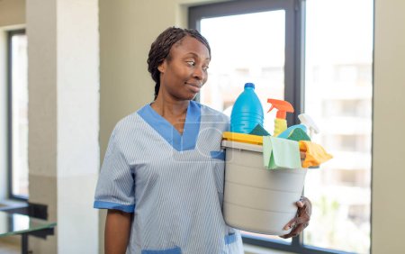Photo for Black afro woman smiling and looking with a happy confident expression with clean products. housekeeper concept - Royalty Free Image