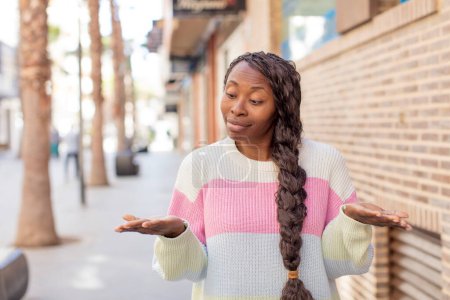 Téléchargez les photos : Afro jolie femme noire tenant un objet avec les deux mains sur l'espace de copie, montrant, offrant ou annonçant un objet - en image libre de droit