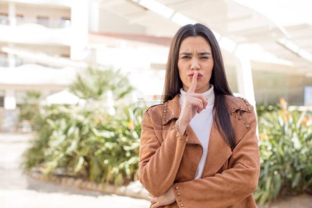 Photo for Pretty young adult woman looking serious and cross with finger pressed to lips demanding silence or quiet, keeping a secret - Royalty Free Image