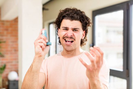 Foto de Joven hombre guapo con un inhalador de asma en el interior del hogar - Imagen libre de derechos