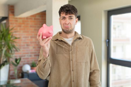 Photo for Young handsome man feeling sad and whiney with an unhappy look and crying. piggy bank concept - Royalty Free Image
