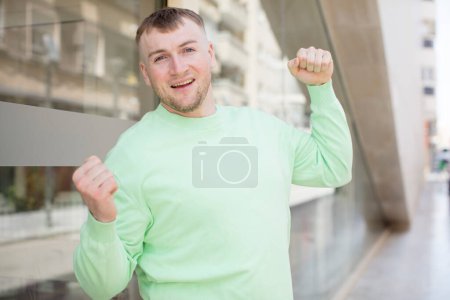 Téléchargez les photos : Bel homme se sentant heureux, positif et réussi, célébrant la victoire, les réalisations ou la bonne chance - en image libre de droit
