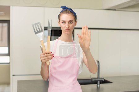 Photo for Looking serious showing open palm making stop gesture. Barbecue tools concept - Royalty Free Image