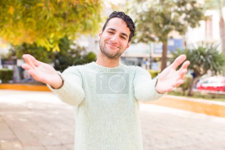 Téléchargez les photos : Jeune homme hispanique souriant joyeusement donnant une accolade chaleureuse, amicale et aimante, se sentant heureux et adorable - en image libre de droit