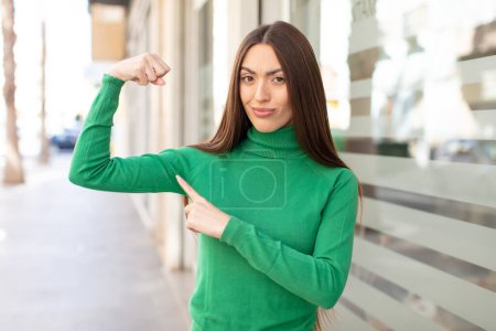 Téléchargez les photos : Jeune jolie femme se sentant heureuse, satisfaite et puissante, en forme fléchissante et biceps musclés, regardant fort après la salle de gym - en image libre de droit