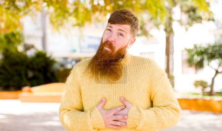 Photo for Red hair bearded man with a goofy, crazy and surprised expression, feeling stuffed, fat and full of food - Royalty Free Image