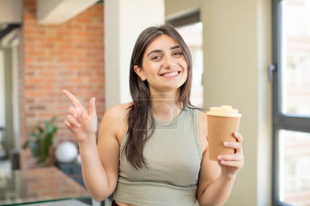 Téléchargez les photos : Jeune femme souriant joyeusement, se sentant heureuse et pointant vers le côté. emporter café - en image libre de droit