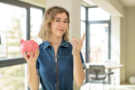 Photo for Pretty woman smiling cheerfully, feeling happy and pointing to the side. piggy bank concept - Royalty Free Image