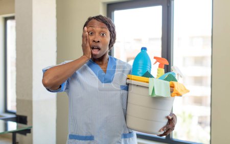 Photo for Black afro woman feeling extremely shocked and surprised with clean products. housekeeper concept - Royalty Free Image
