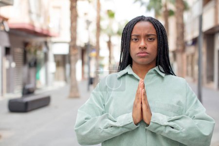 Photo for Afro pretty black woman feeling worried, hopeful and religious, praying faithfully with palms pressed, begging forgiveness - Royalty Free Image