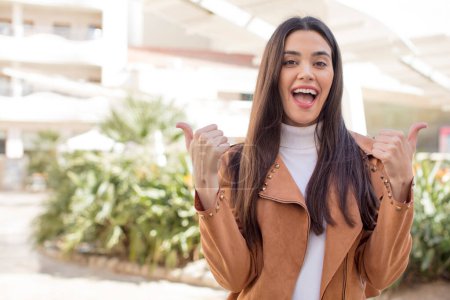 Foto de Pretty young adult woman smiling joyfully and looking happy, feeling carefree and positive with both thumbs up - Imagen libre de derechos