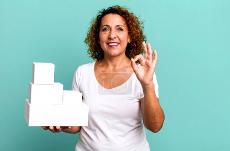 Foto de Mujer bastante mediana edad sentirse feliz, mostrando aprobación con gesto bien. cajas blancas en blanco embalaje - Imagen libre de derechos