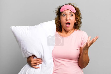 Photo for Pretty middle age woman feeling extremely shocked and surprised wearing pajamas night wear and a pillow - Royalty Free Image