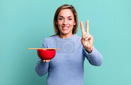 Photo for Pretty blonde woman smiling and looking friendly, showing number two. japanese noodles concept - Royalty Free Image