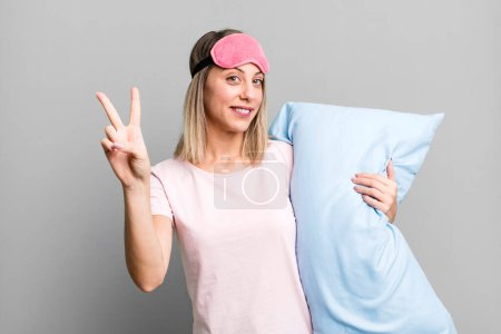Photo for Pretty blonde woman smiling and looking happy, gesturing victory or peace. pajamas and nightwear concept - Royalty Free Image