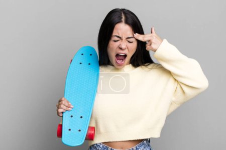 Foto de Mujer bonita hispana que parece infeliz y estresada, gesto suicida haciendo señal de arma. concepto de skate boarding - Imagen libre de derechos