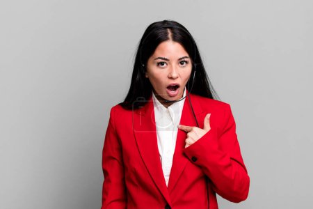 Photo for Hispanic pretty woman looking shocked and surprised with mouth wide open, pointing to self. telemarketing concept - Royalty Free Image