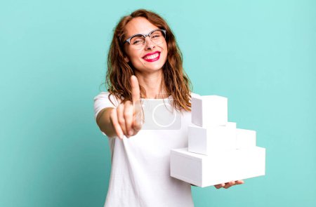Photo for Hispanic pretty woman smiling proudly and confidently making number one. with white boxes packages - Royalty Free Image