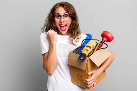 Photo for Hispanic pretty woman feeling shocked,laughing and celebrating success with a tool box. handyman concept - Royalty Free Image